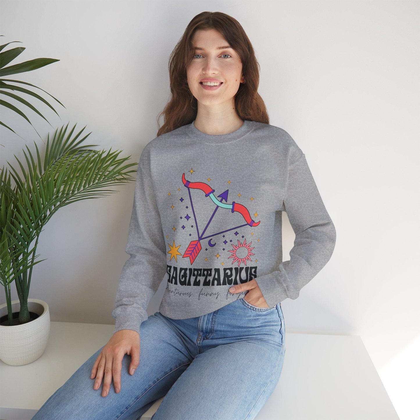 A vintage light blue colored Gildan sweatshirt features a large red and purple bow and arrow surrounded by stars and the sun with the text Sagittarius in large bold font and below that are the words adventurous, funny, forgiving in cursive font.