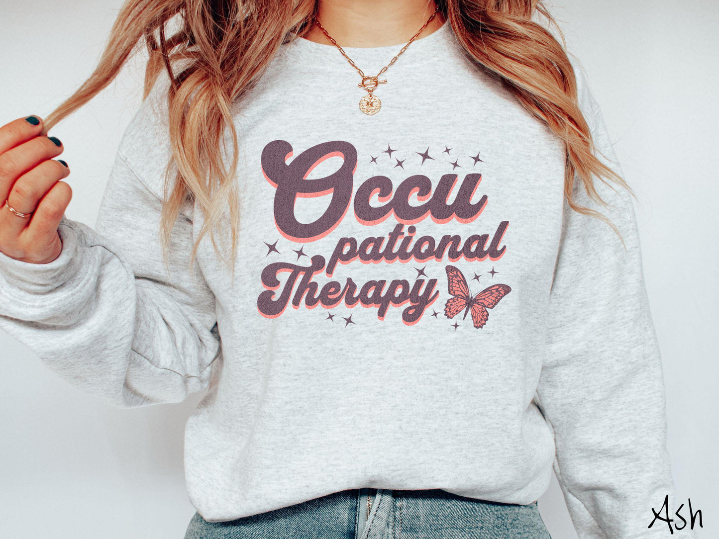 A vintage, ash colored Gildan sweatshirt featuring the words Occupational Therapy across the front, this unique design showcases a stunning pink and dark purple butterfly surrounded by delicate twinkling stars.
