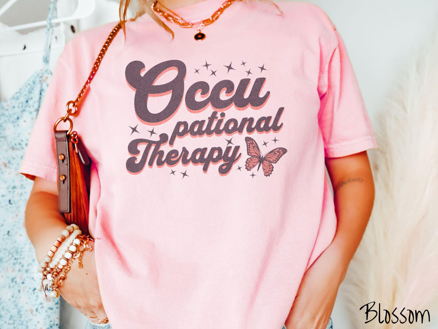 A vintage, blossom colored Comfort Colors t-shirt featuring the words Occupational Therapy across the front, this unique design showcases a stunning pink and dark purple butterfly surrounded by delicate twinkling stars.