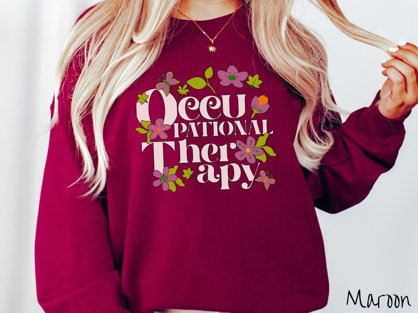 A vintage, maroon colored Gildan sweatshirt with the text Occupational Therapy and featuring green leaves, purple and orange flowers, and colorful butterflies in the background.