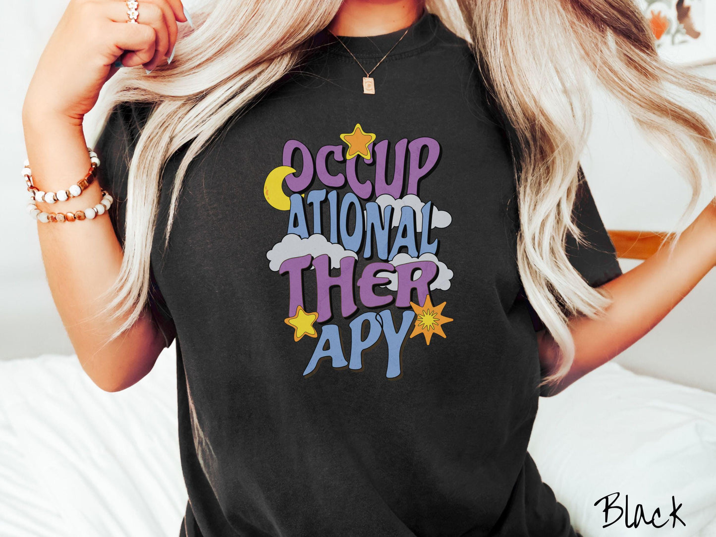A vintage, black colored Comfort Colors t-shirt with the text Occupational Therapy vertically with clouds, the yellow moon, and bright yellow and orange stars mixed in.