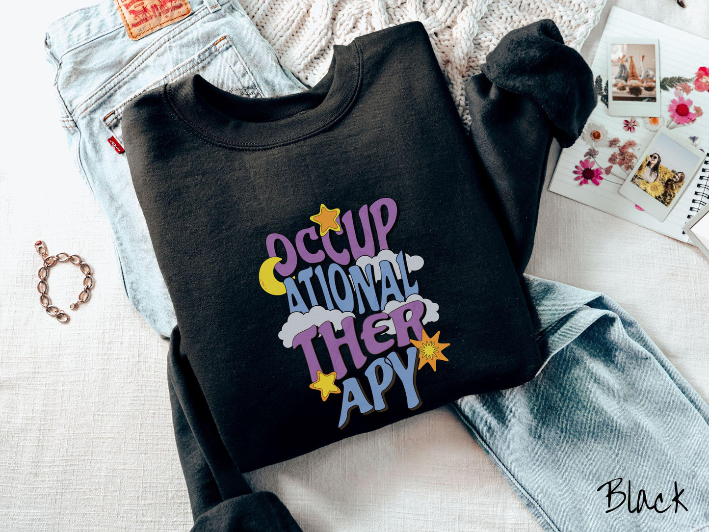 A vintage, black colored Gildan sweatshirt with the text Occupational Therapy vertically with clouds, the yellow moon, and bright yellow and orange stars mixed in.