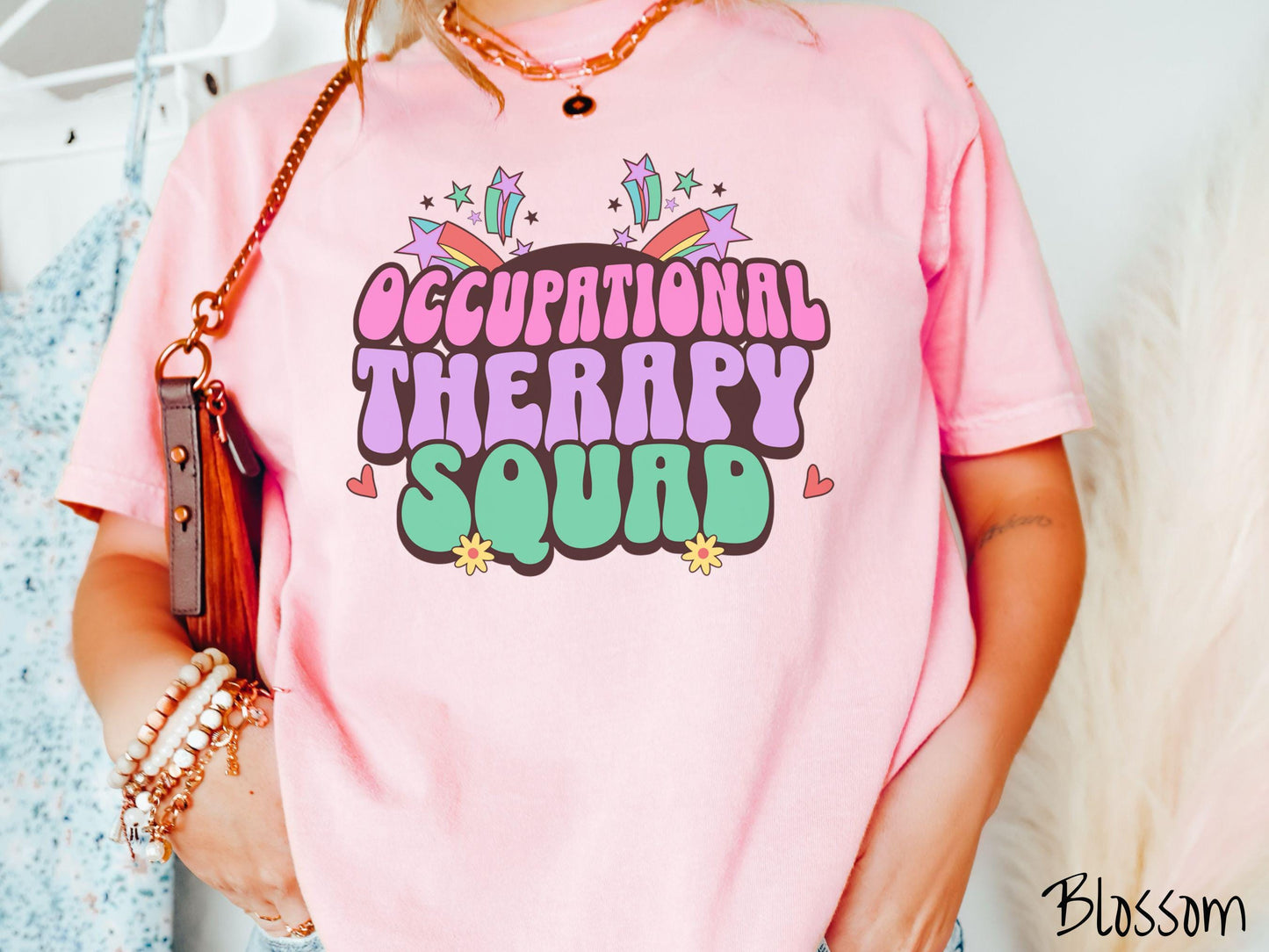 A vintage, blossom colored Comfort Colors T-shirt with the text Occupational Therapy Squad in colorful font with red hearts, sunflowers, and shooting stars mixed in.