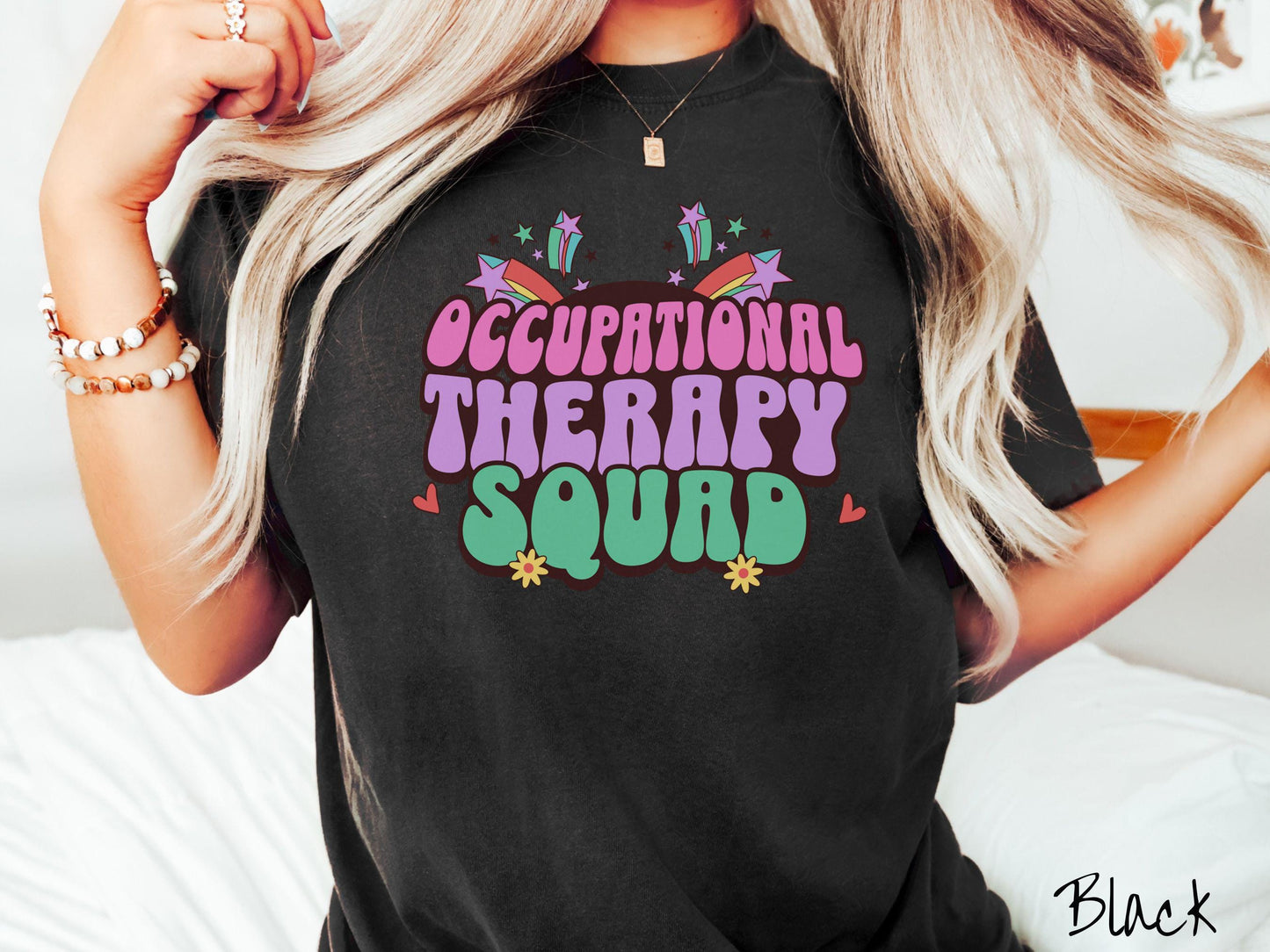 A vintage, black colored Comfort Colors T-shirt with the text Occupational Therapy Squad in colorful font with red hearts, sunflowers, and shooting stars mixed in.