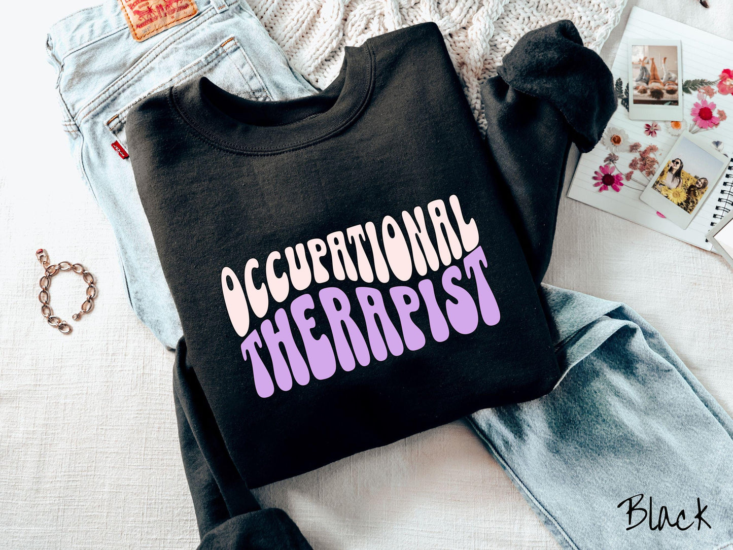 A vintage, black colored Gildan sweatshirt featuring the text Occupational Therapist in fun wavy font. This sweater is perfect for occupational therapists looking to add a touch of personality to their casual or semi-formal outfits.
