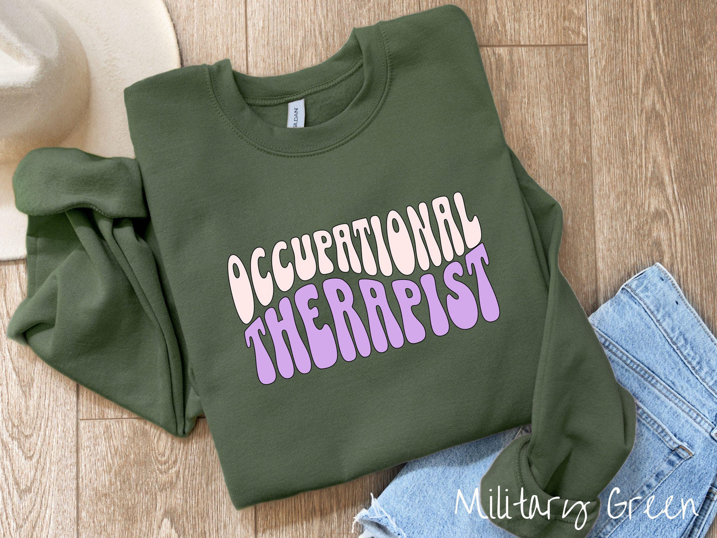A vintage, military green colored Gildan sweatshirt featuring the text Occupational Therapist in fun wavy font. This sweater is perfect for occupational therapists looking to add a touch of personality to their casual or semi-formal outfits.