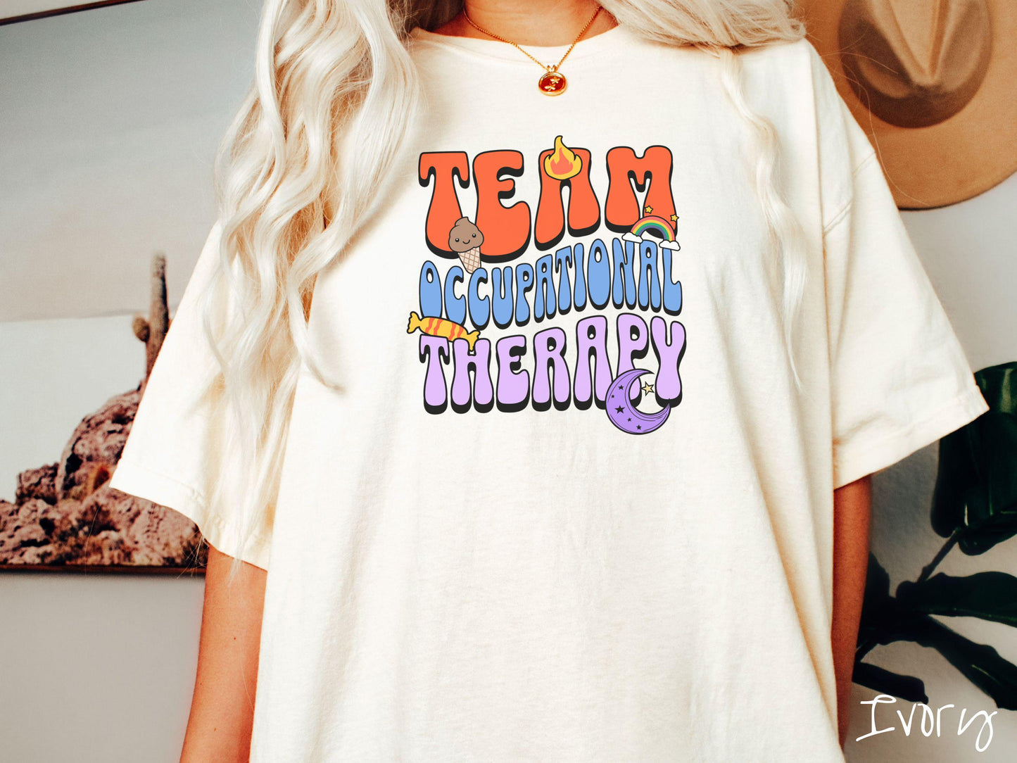 A vintage, ivory colored Comfort Colors t-shirt with the text "Team Occupational Therapy" surrounded by playful elements like a chocolate ice cream cone, a blazing flame, a colorful rainbow, a piece of candy, and a serene moon.