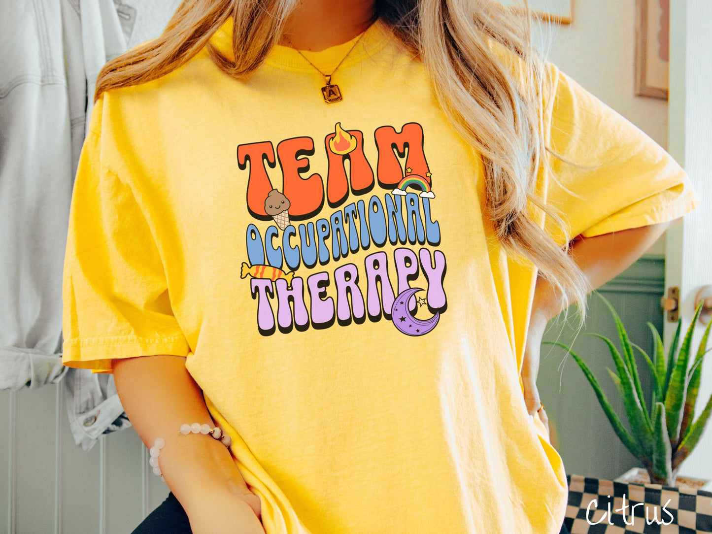 A vintage, citrus colored Comfort Colors t-shirt with the text "Team Occupational Therapy" surrounded by playful elements like a chocolate ice cream cone, a blazing flame, a colorful rainbow, a piece of candy, and a serene moon.