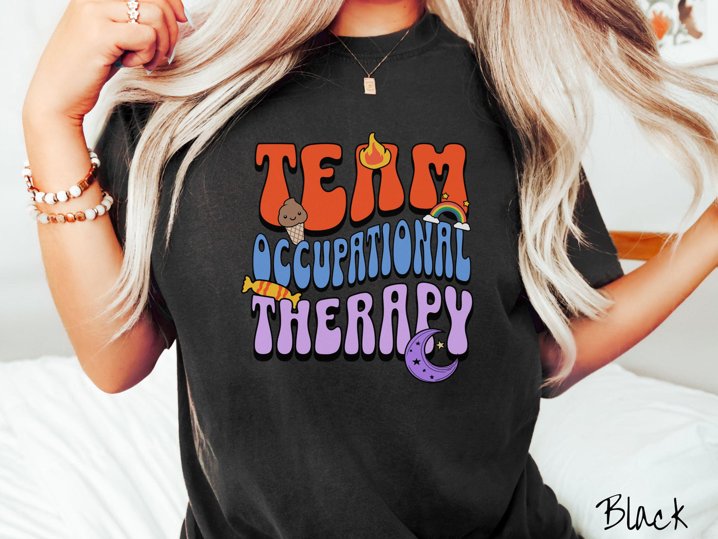 A vintage, black colored Comfort Colors t-shirt with the text "Team Occupational Therapy" surrounded by playful elements like a chocolate ice cream cone, a blazing flame, a colorful rainbow, a piece of candy, and a serene moon.