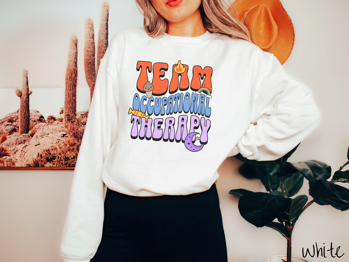 A vintage, white colored Gildan sweatshirt with the text "Team Occupational Therapy" surrounded by playful elements like a chocolate ice cream cone, a blazing flame, a colorful rainbow, a piece of candy, and a serene moon.