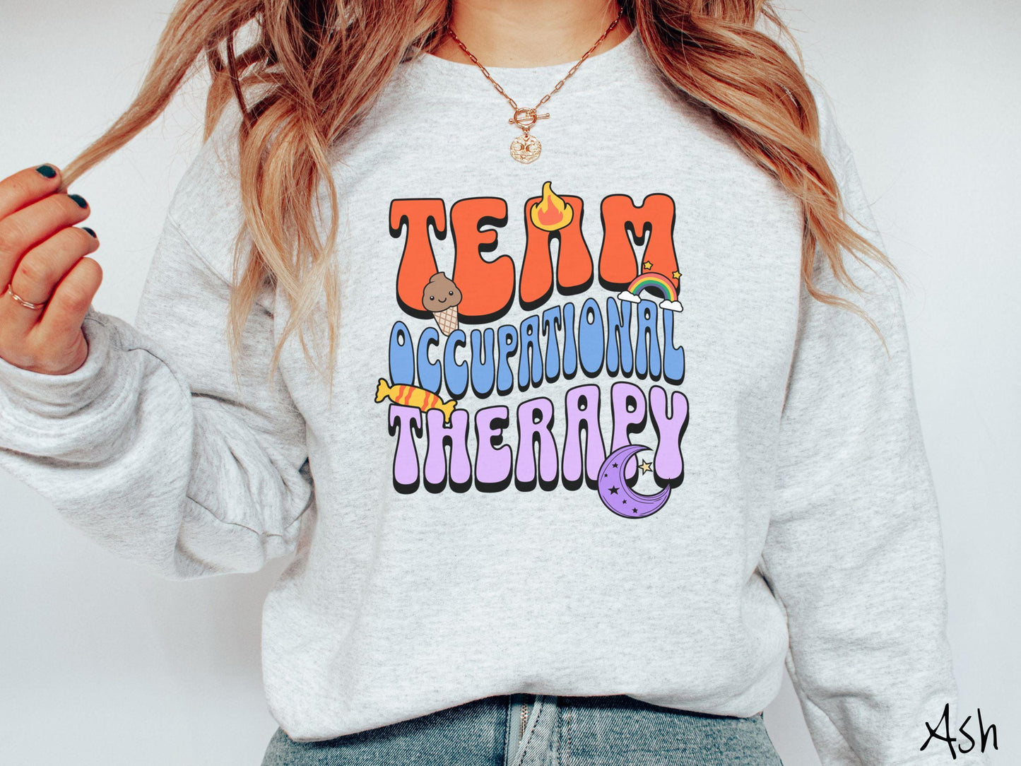 A vintage, ash colored Gildan sweatshirt with the text "Team Occupational Therapy" surrounded by playful elements like a chocolate ice cream cone, a blazing flame, a colorful rainbow, a piece of candy, and a serene moon.