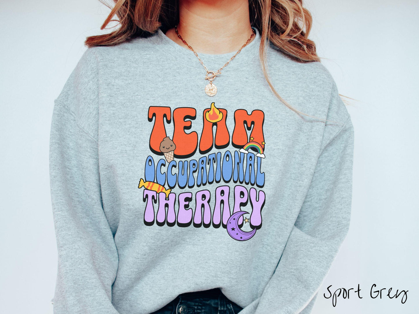 A vintage, sport grey colored Gildan sweatshirt with the text "Team Occupational Therapy" surrounded by playful elements like a chocolate ice cream cone, a blazing flame, a colorful rainbow, a piece of candy, and a serene moon.