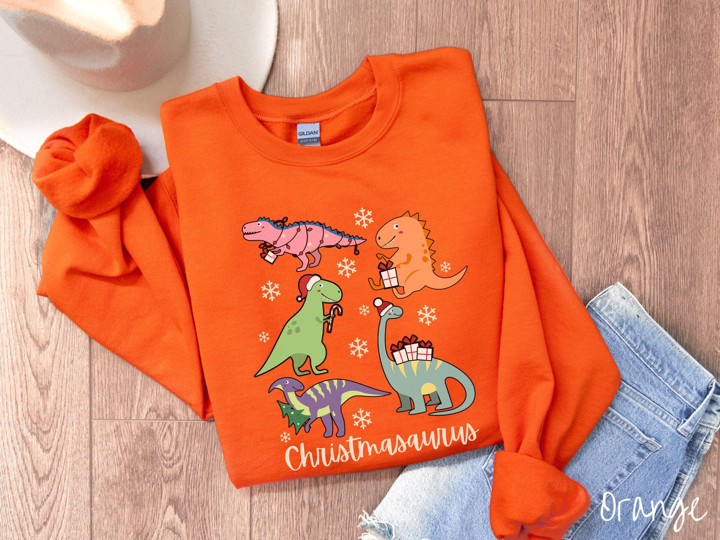 An adorable orange colored Christmasaurus Gildan sweatshirt. Featuring a variety of colorful dinosaurs dressed up for the holidays, this sweater exudes a playful and cheerful vibe.