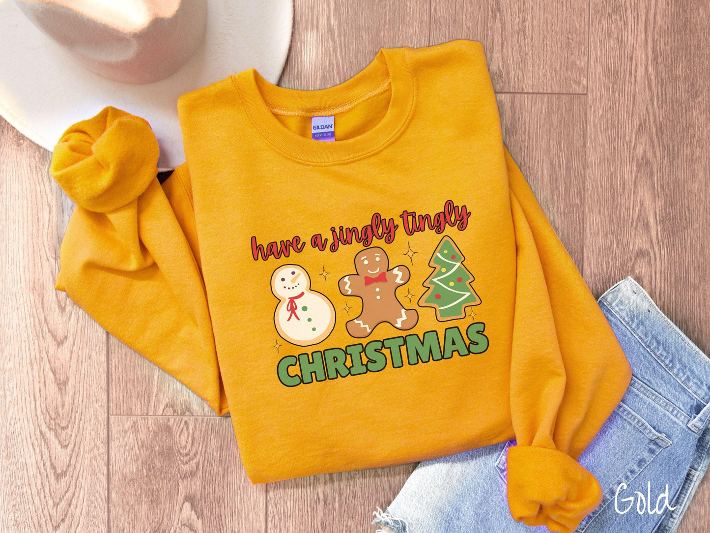 A vintage gold colored Christmas Gildan sweatshirt featuring a snowman iced cookie, a gingerbread man cookie, and a Christmas tree cookie. The text reads 'have a jingly tingly Christmas' in red and green font.