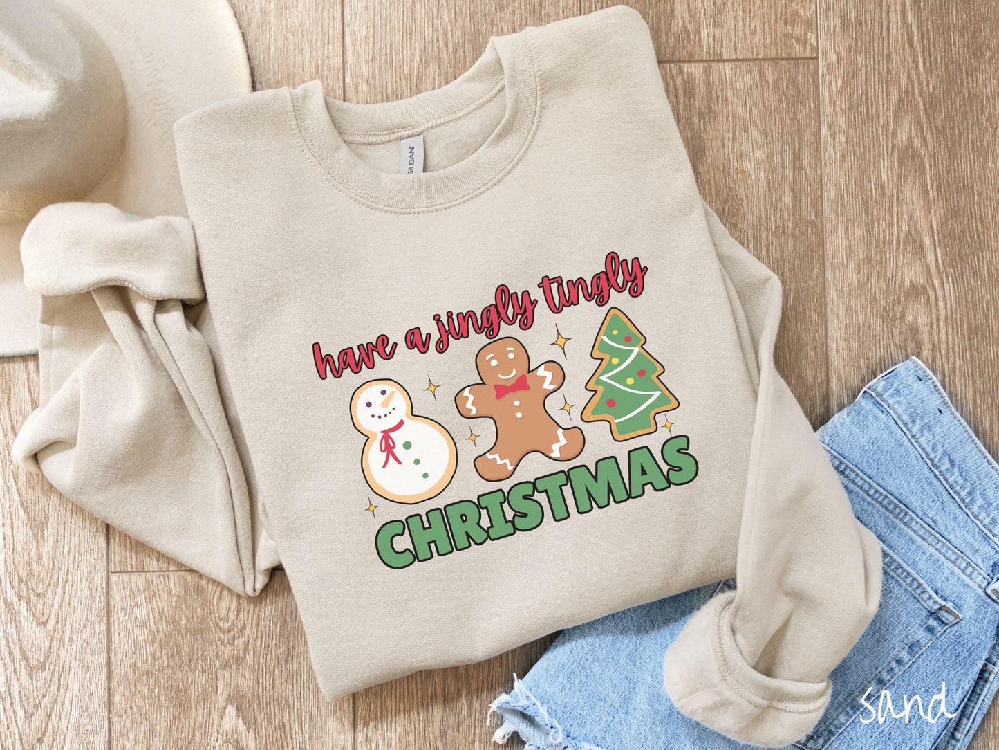 A vintage sand colored Christmas Gildan sweatshirt featuring a snowman iced cookie, a gingerbread man cookie, and a Christmas tree cookie. The text reads 'have a jingly tingly Christmas' in red and green font.