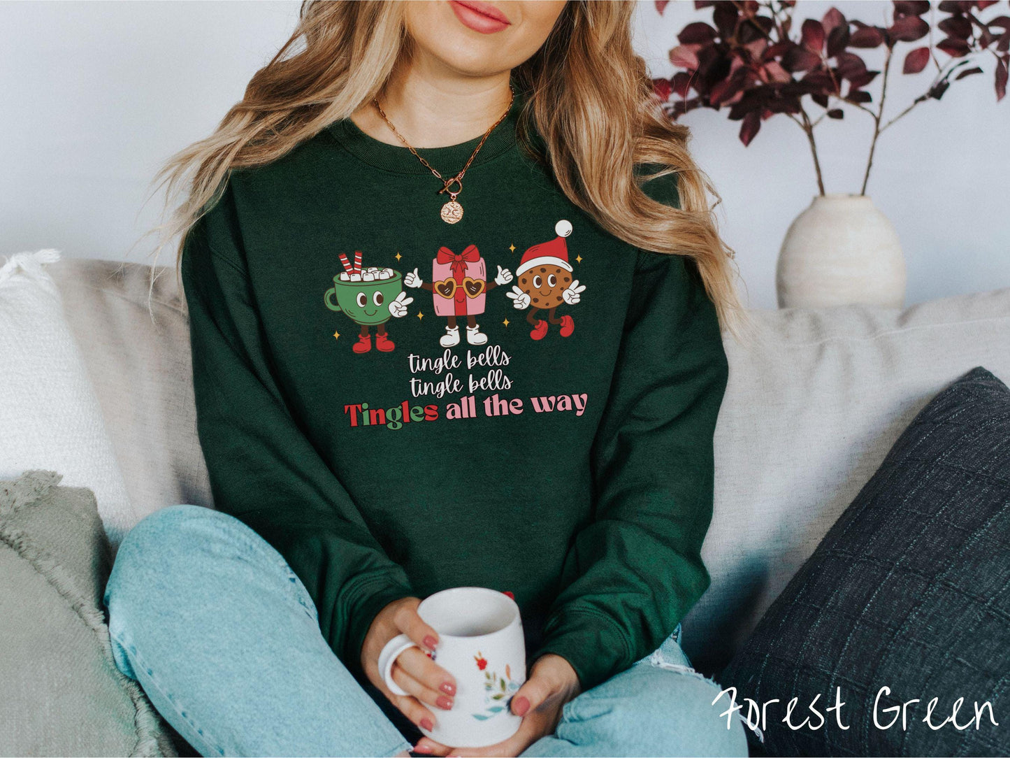 A cute, vintage forest green colored Gildan sweatshirt with text tingle bells, tingle bells, Tingles all the way. Above are a green cup of hot cocoa, a red present wearing heart-shaped glasses, and a chocolate chip cookie wearing a Santa hat.