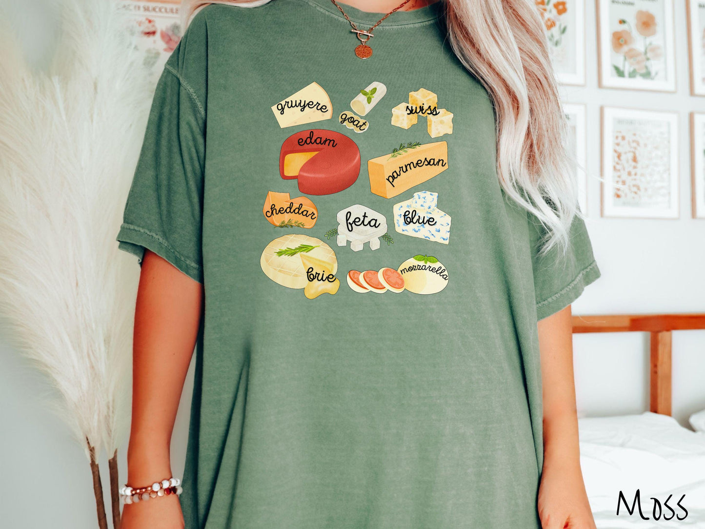A vintage moss colored T-shirt is perfect for cheese lovers with a grid pattern of various cheeses like feta, parmesan, gruyere, goat, swiss, edam, cheddar, blue, brie, and mozzarella listed.