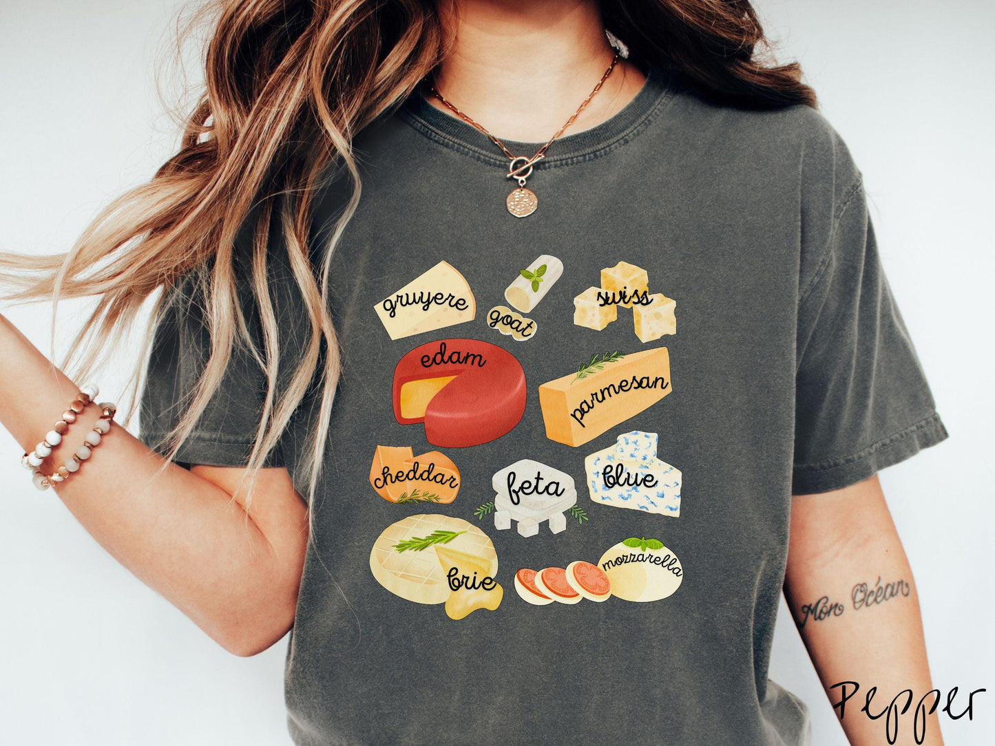 A vintage pepper colored T-shirt is perfect for cheese lovers with a grid pattern of various cheeses like feta, parmesan, gruyere, goat, swiss, edam, cheddar, blue, brie, and mozzarella listed.