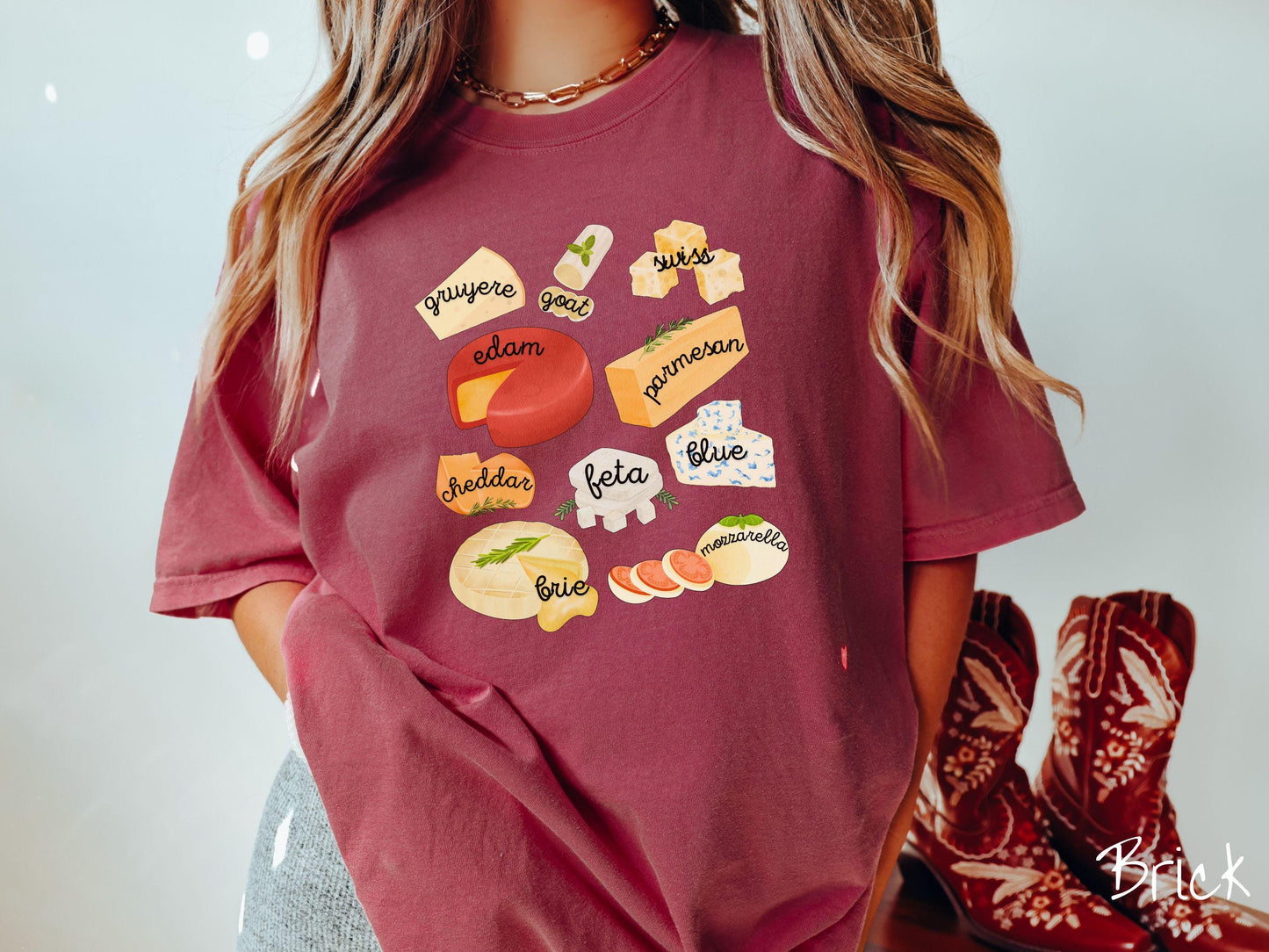 A vintage brick colored T-shirt is perfect for cheese lovers with a grid pattern of various cheeses like feta, parmesan, gruyere, goat, swiss, edam, cheddar, blue, brie, and mozzarella listed.