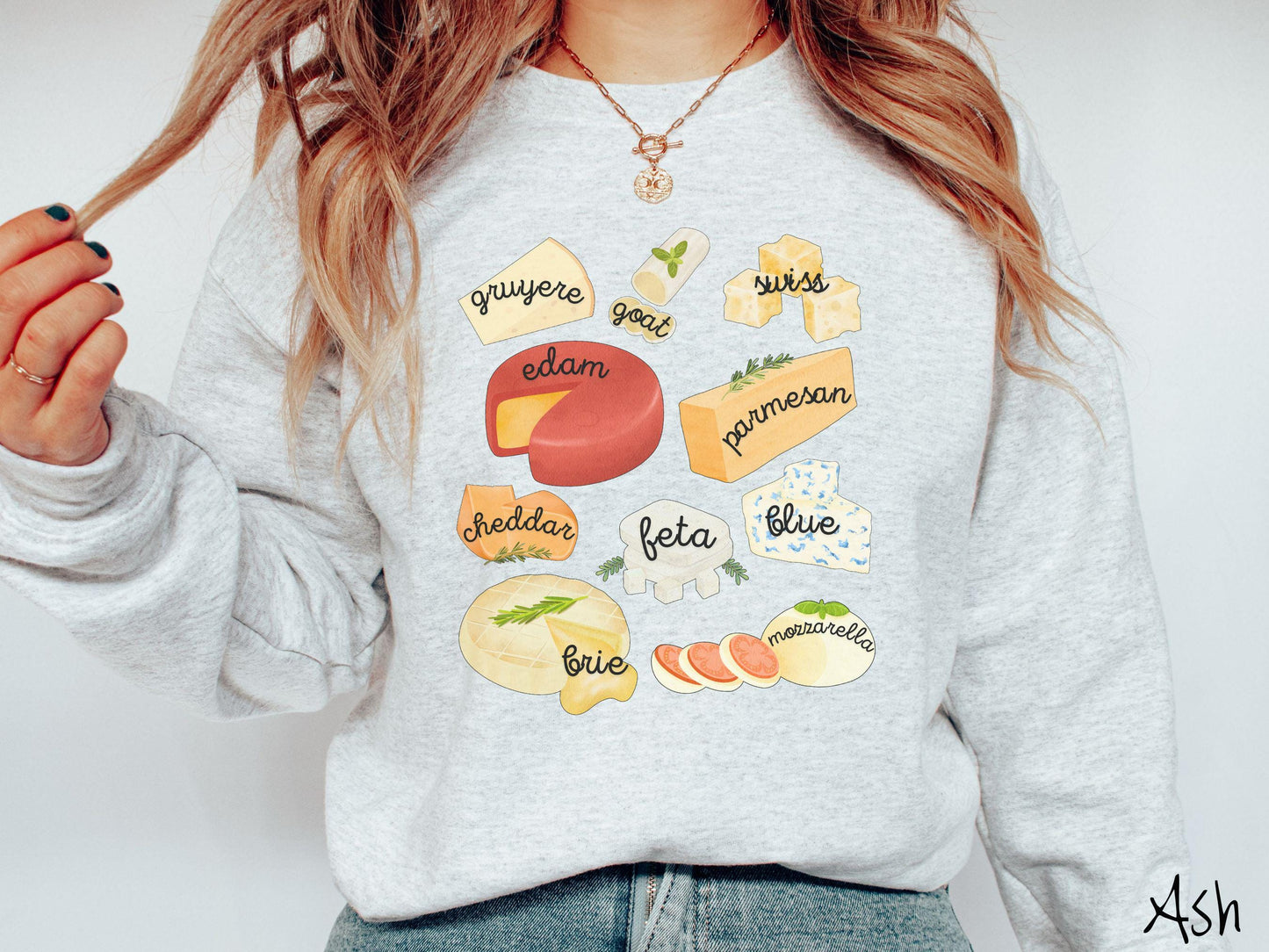 A vintage ash colored Gildan sweatshirt is perfect for cheese lovers with a grid pattern of various cheeses like feta, parmesan, gruyere, goat, swiss, edam, cheddar, blue, brie, and mozzarella listed.