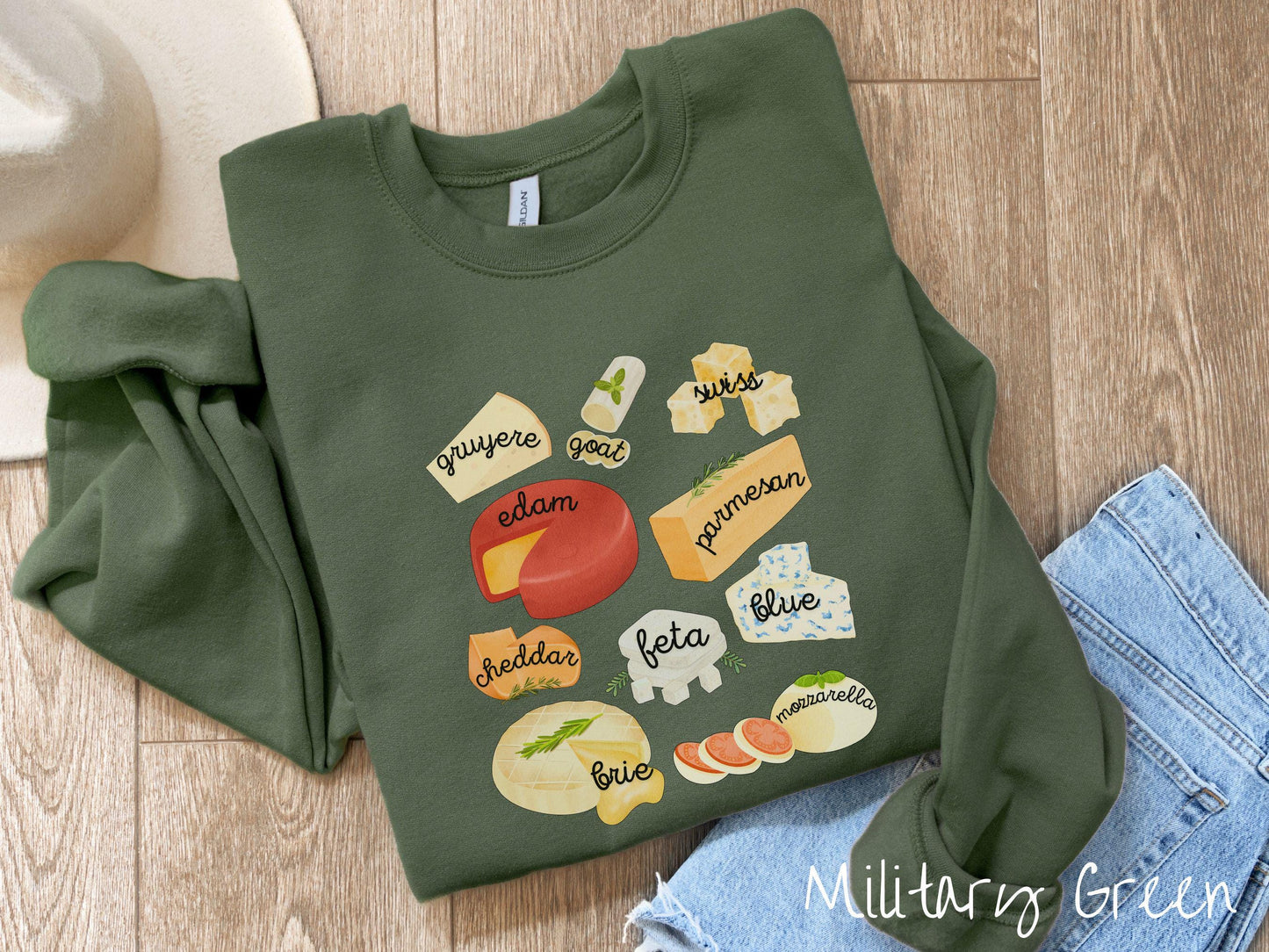 A vintage military green colored Gildan sweatshirt is perfect for cheese lovers with a grid pattern of various cheeses like feta, parmesan, gruyere, goat, swiss, edam, cheddar, blue, brie, and mozzarella listed.