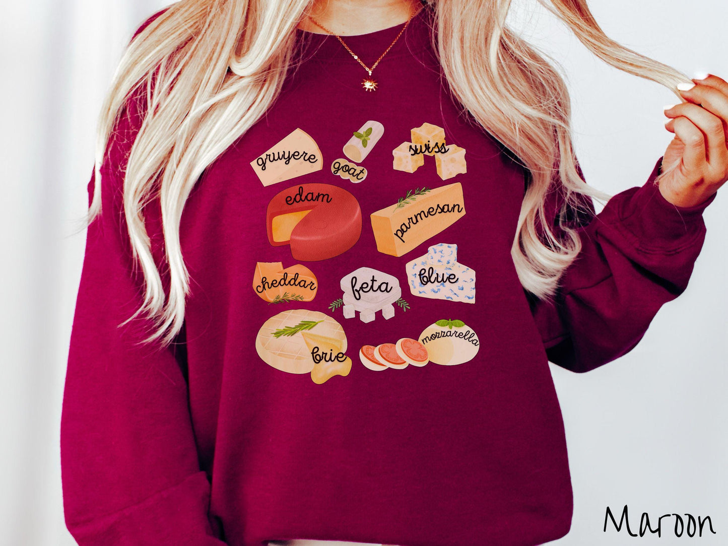 A vintage maroon colored Gildan sweatshirt is perfect for cheese lovers with a grid pattern of various cheeses like feta, parmesan, gruyere, goat, swiss, edam, cheddar, blue, brie, and mozzarella listed.