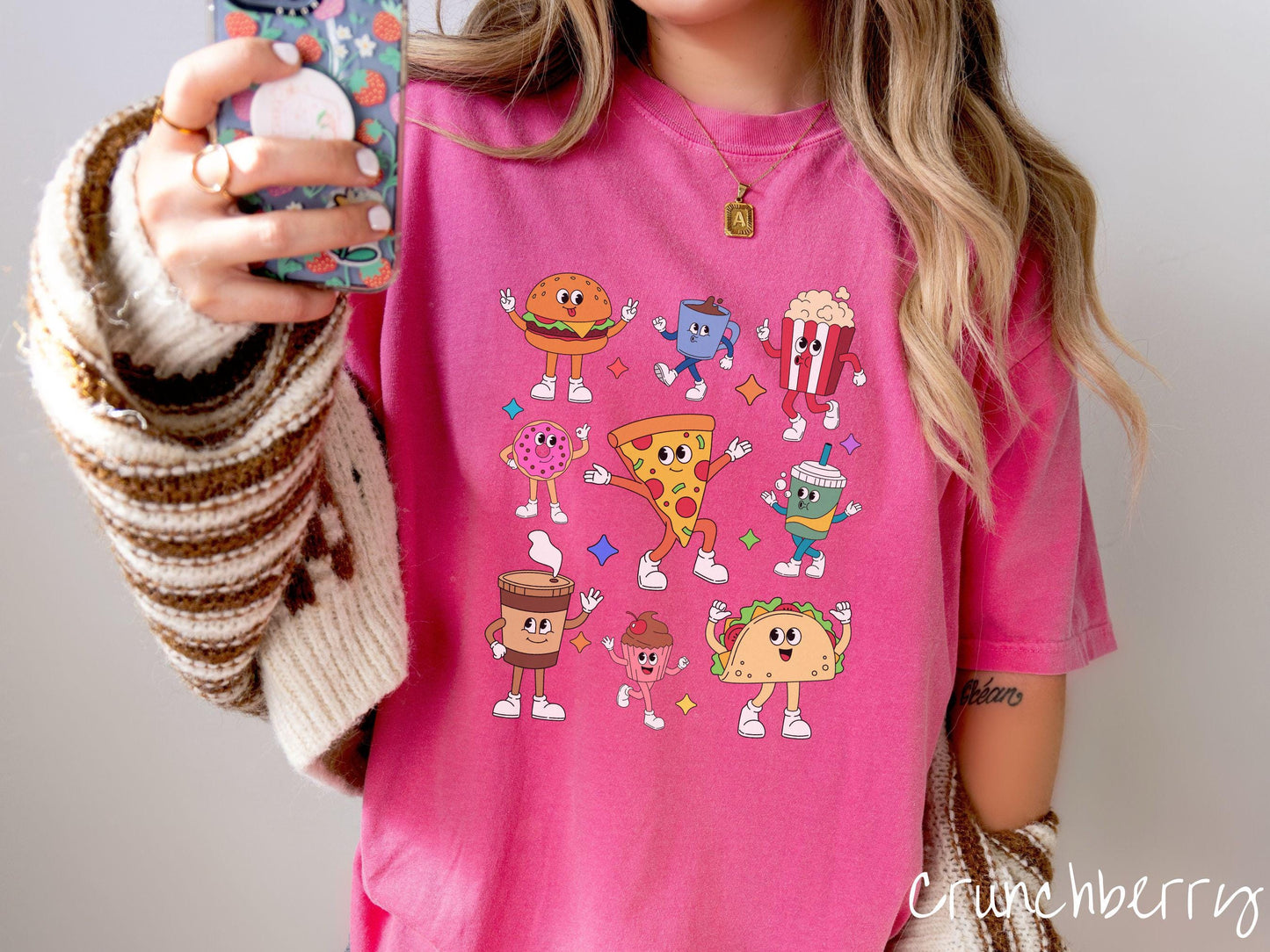 A vintage crunchberry colored Comfort Colors t-shirt featuring a grid style design of assorted junk foods like a cheeseburger, popcorn, donut, pizza, and a taco, all with smiling faces inside with white gloved hands holding up hand gestures.