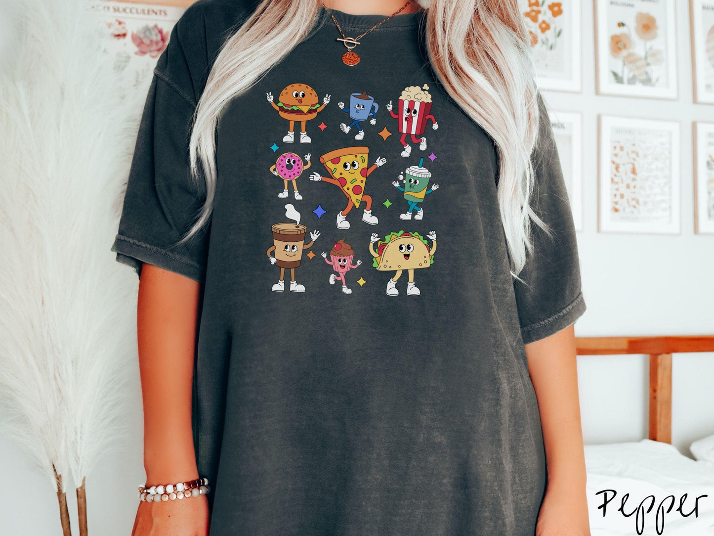 A vintage pepper colored Comfort Colors t-shirt featuring a grid style design of assorted junk foods like a cheeseburger, popcorn, donut, pizza, and a taco, all with smiling faces inside with white gloved hands holding up hand gestures.
