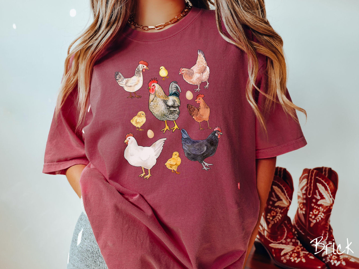 A vintage brick colored Comfort Colors t-shirt featuring a grid style design of assorted colorful chickens, hens, and roosters in a grid design, with chicken eggs scattered among the design.