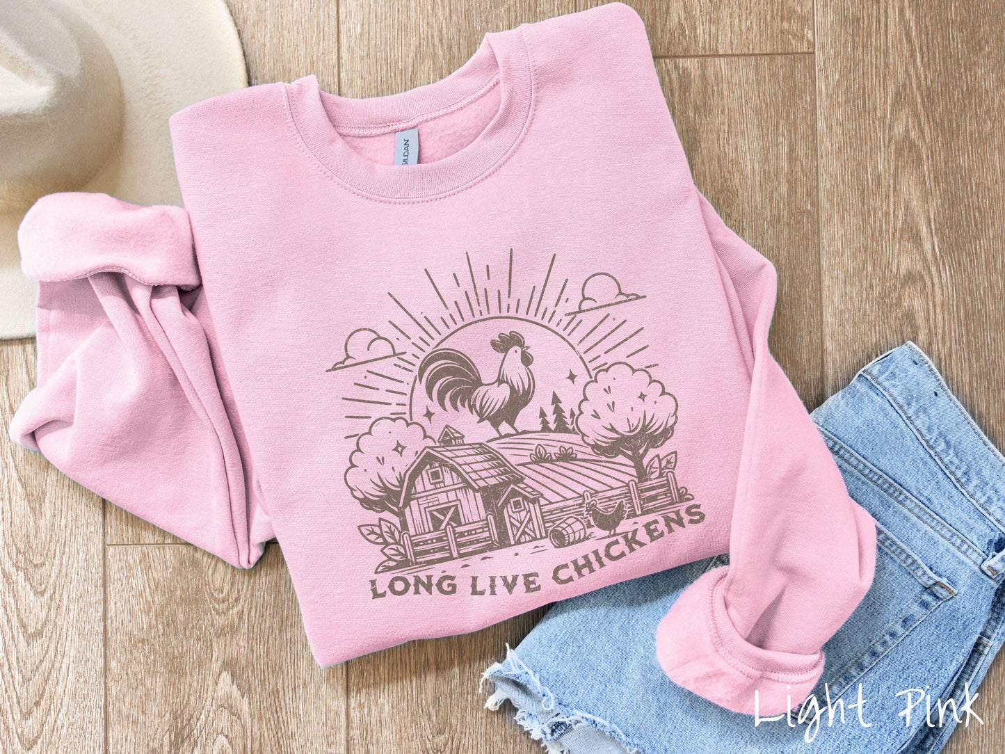 A vintage light pink colored Gildan sweatshirt featuring a design of a farm with a fence, trees, and plants scattered along the property, a huge chicken in the background at the top of a pasture in front of the sun, and text Long Live Chickens.