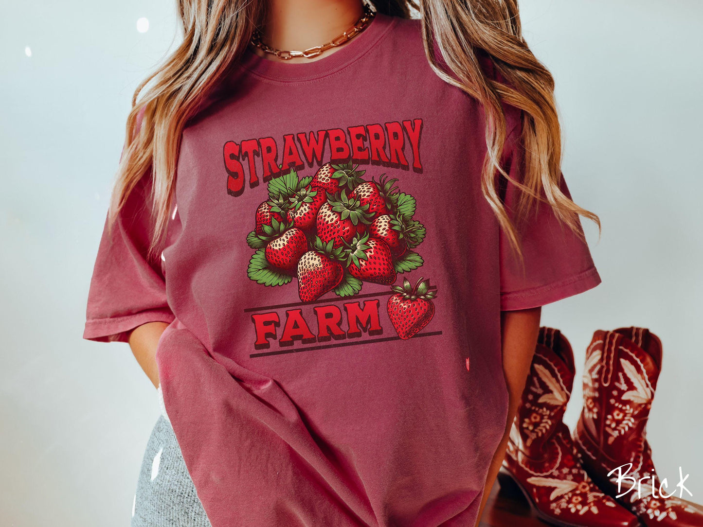 A vintage brick colored Comfort Colors t-shirt featuring the text Strawberry Farm in red font with a bundle of red strawberries in between the text.