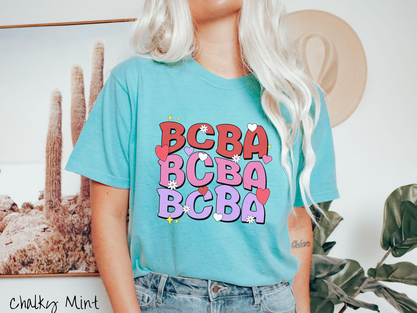 A vibrant Comfort Colors T-shirt with the text BCBA written three times vertically, accompanied by tiny hearts, stars, and flowers. Perfect for Board Certified Behavior Analysts, this tee is a great Valentine's Day gift to show appreciation and love.