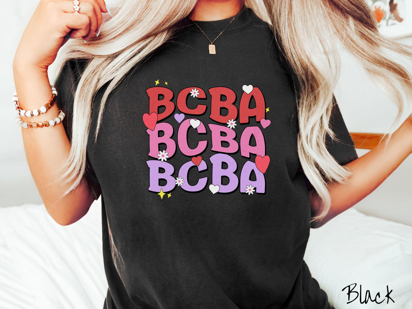 A vibrant Comfort Colors T-shirt with the text BCBA written three times vertically, accompanied by tiny hearts, stars, and flowers. Perfect for Board Certified Behavior Analysts, this tee is a great Valentine's Day gift to show appreciation and love.