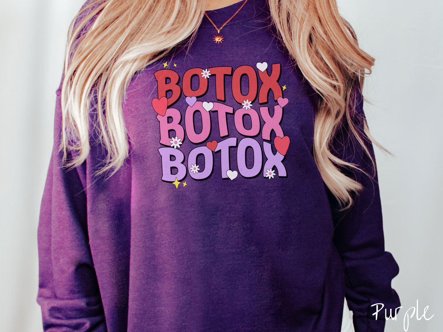 A vibrant Gildan sweatshirt with the text BOTOX written three times vertically, accompanied by tiny hearts, stars, and flowers. The perfect gift for friends who are into cosmetic botox nursing.