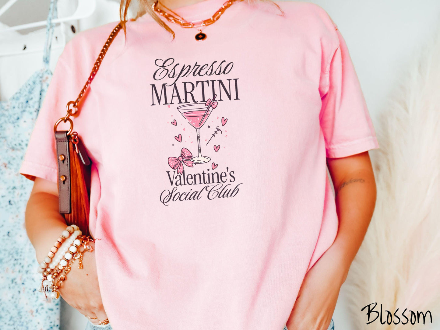 A stylish Comfort Colors T-shirt featuring the phrase "Espresso Martini" above a martini glass filled with pink martini a pink bow-topped toothpick. The words "Valentine's Social Club" appear below, with pink bows and hearts throughout the design.