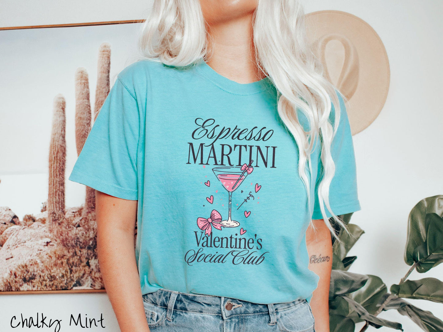 A stylish Comfort Colors T-shirt featuring the phrase "Espresso Martini" above a martini glass filled with pink martini a pink bow-topped toothpick. The words "Valentine's Social Club" appear below, with pink bows and hearts throughout the design.