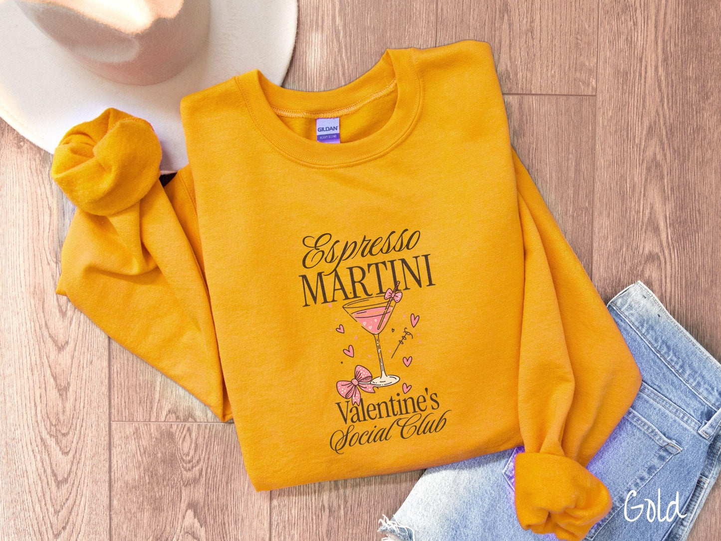 A stylish Gildan sweatshirt featuring the phrase "Espresso Martini" above a martini glass filled with pink martini and a pink bow-topped toothpick. The words "Valentine's Social Club" appear below with pink bows and hearts throughout the design.