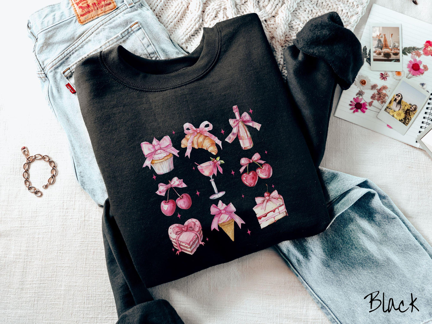 A stylish coquette Gildan sweatshirt featuring a grid of assorted treats with pink ribbons like a cupcake, a croissant, a champaigne bottle, cherries, a pink martini, a pink cake, and a pink ince cream cone, along with twinkling pink stars.