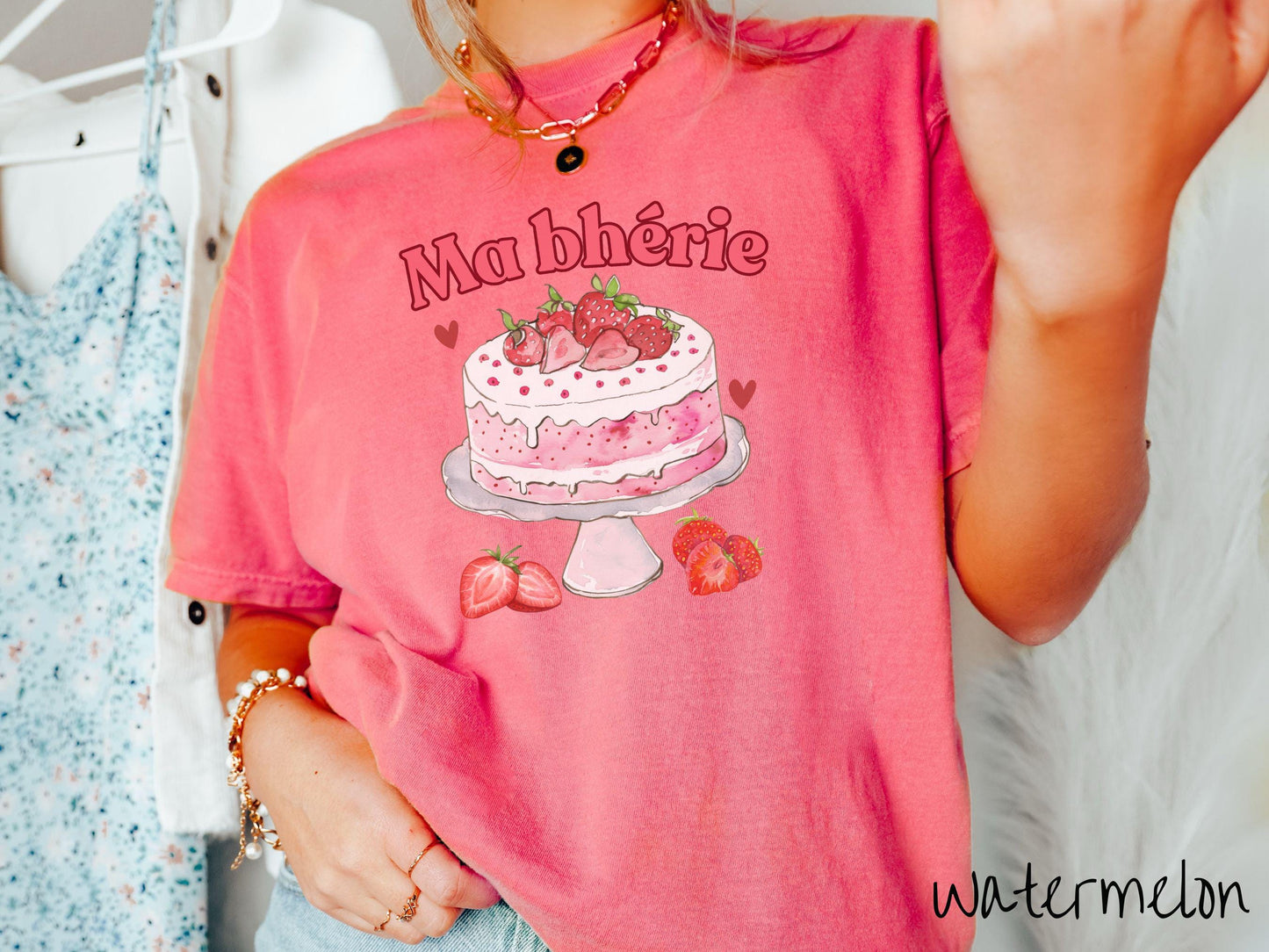 A Comfort Colors T-shirt featuring the phrase "Ma Bherie" is printed in bold red font above a charming illustration of a red-and-white strawberry cake displayed on a plate, topped with fresh strawberries and surrounded by even more berries.