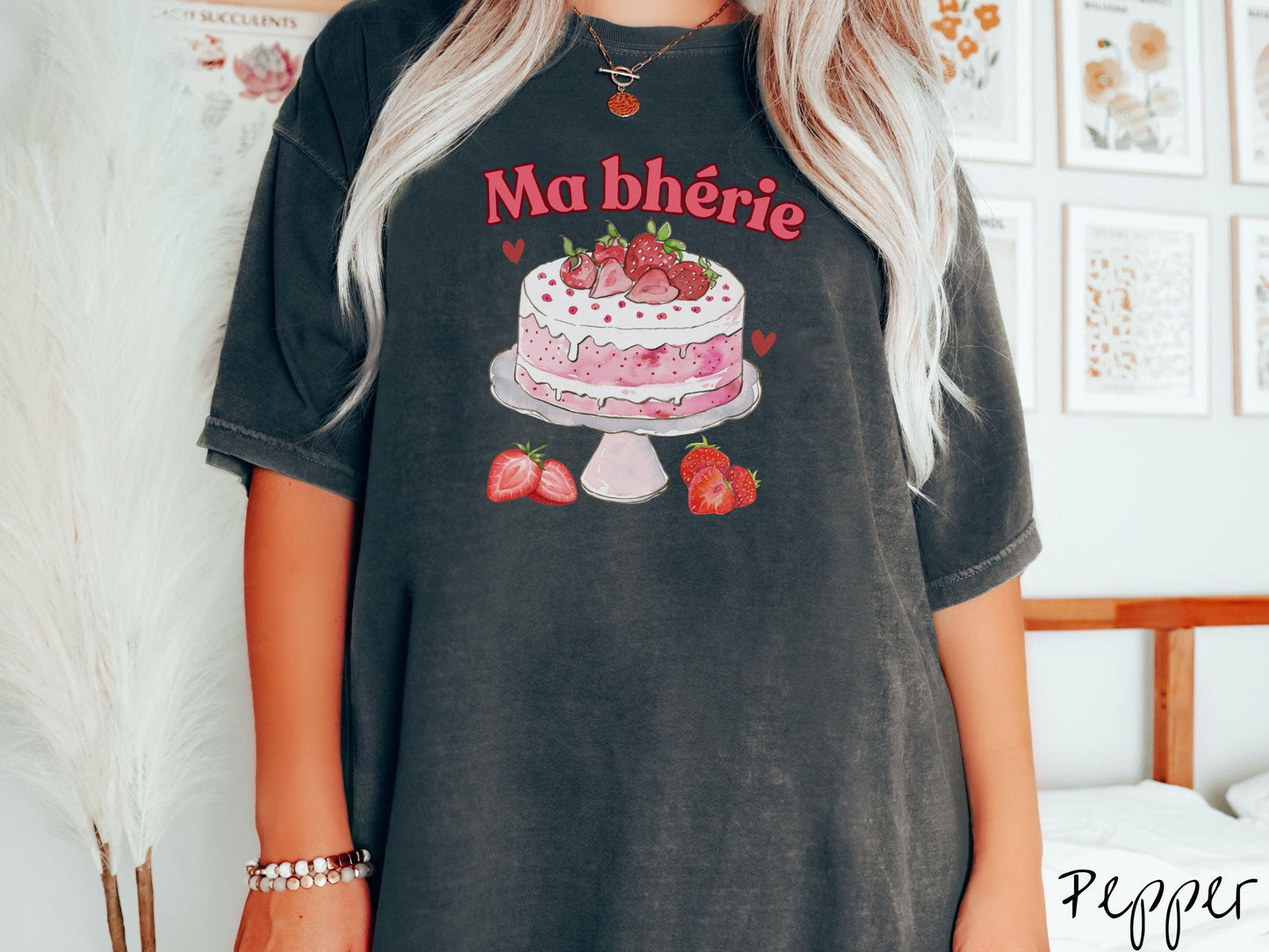 A Comfort Colors T-shirt featuring the phrase "Ma Bherie" is printed in bold red font above a charming illustration of a red-and-white strawberry cake displayed on a plate, topped with fresh strawberries and surrounded by even more berries.
