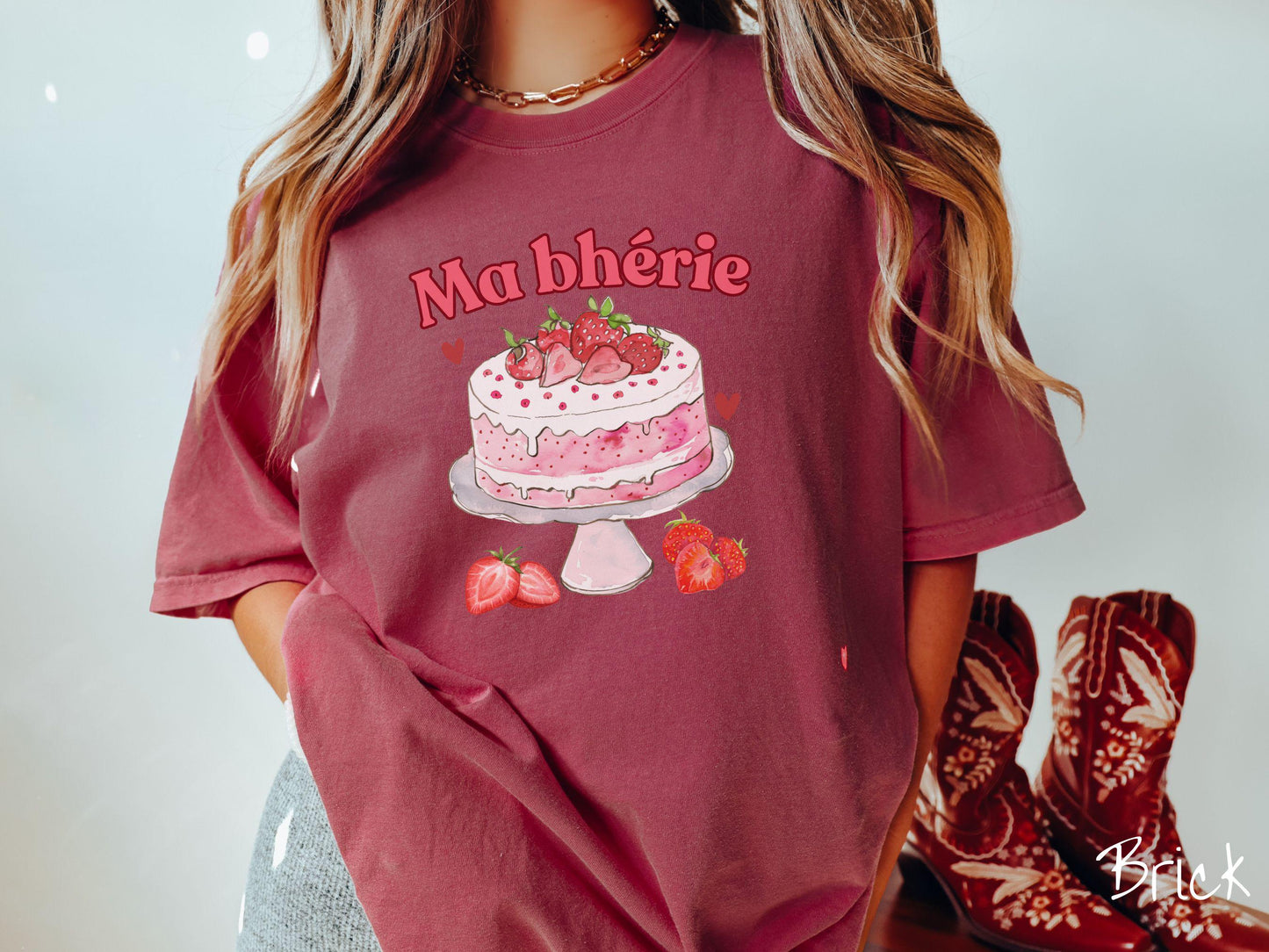 A Comfort Colors T-shirt featuring the phrase "Ma Bherie" is printed in bold red font above a charming illustration of a red-and-white strawberry cake displayed on a plate, topped with fresh strawberries and surrounded by even more berries.