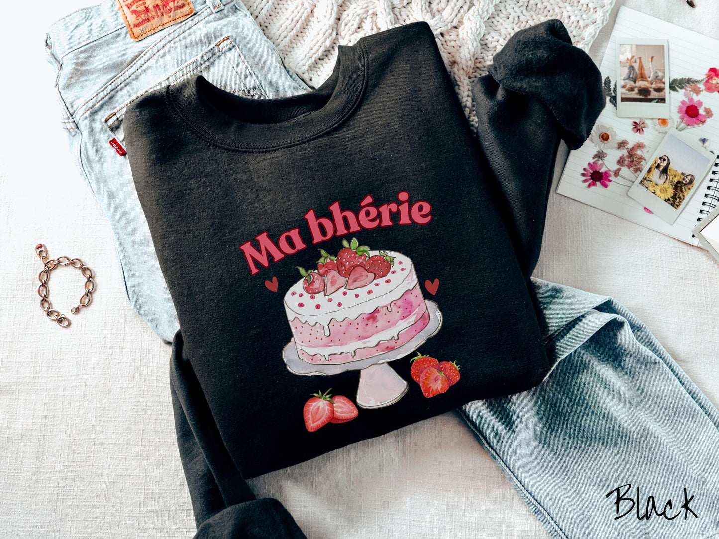 A Gildan sweatshirt featuring the phrase "Ma Bherie" is printed in bold red font above a charming illustration of a red-and-white strawberry cake displayed on a plate, topped with fresh strawberries and surrounded by even more berries.