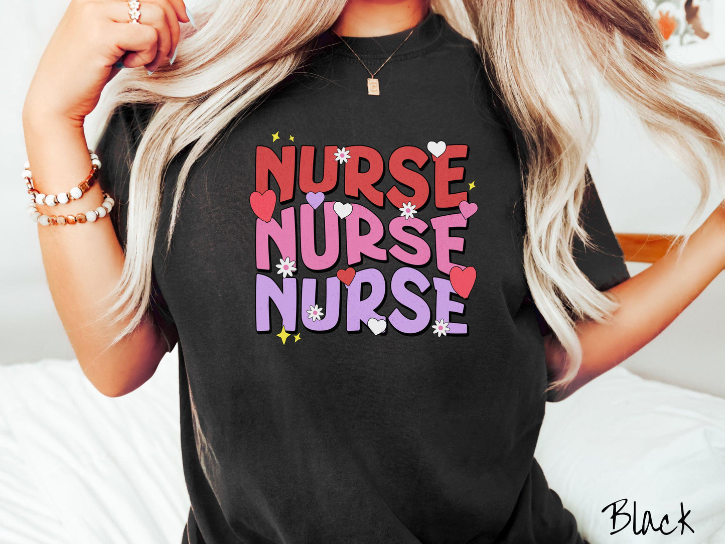 A stylish Comfort Colors T-shirt featuring the word "NURSE" written three times vertically in red, pink, and purple font. There are red, white, and purple hearts mixed into the design as well as yellow twinkling stars.