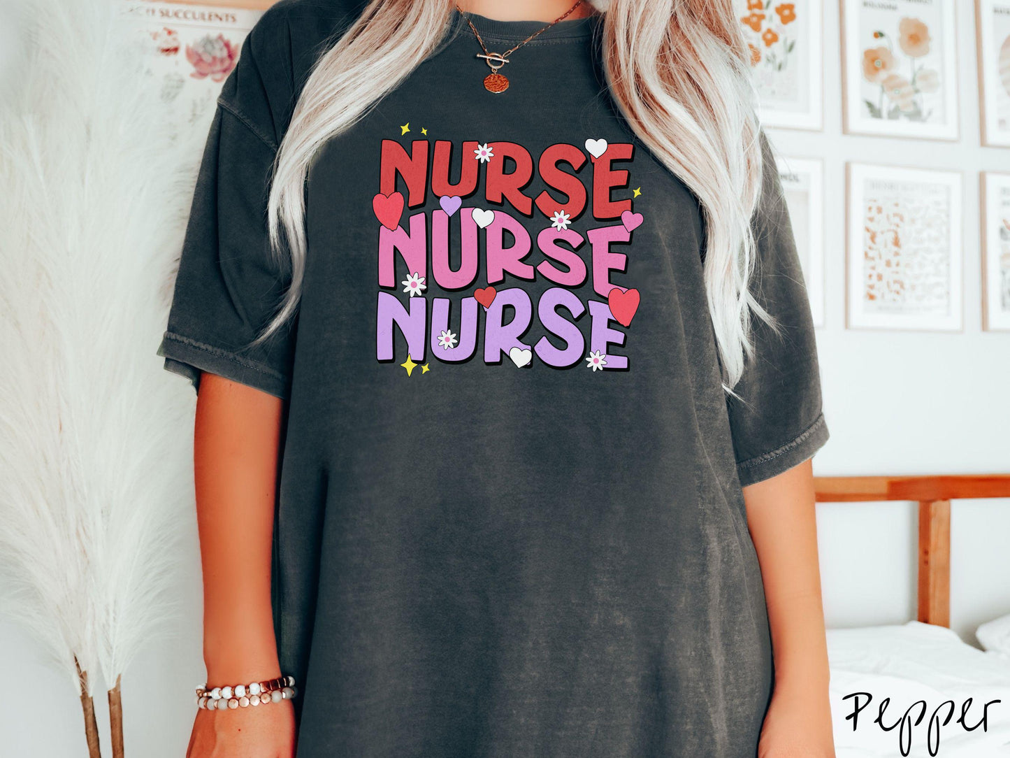 A stylish Comfort Colors T-shirt featuring the word "NURSE" written three times vertically in red, pink, and purple font. There are red, white, and purple hearts mixed into the design as well as yellow twinkling stars.