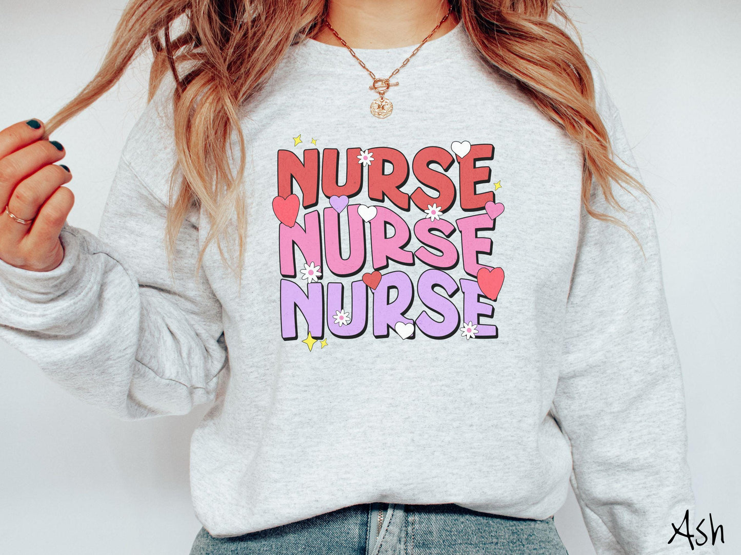 A stylish Gildan Sweatshirt featuring the word "NURSE" written three times vertically in red, pink, and purple font. There are red, white, and purple hearts mixed into the design as well as yellow twinkling stars.