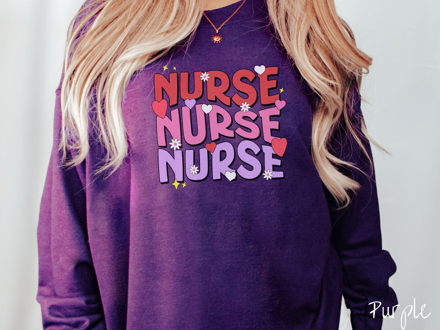 A stylish Gildan Sweatshirt featuring the word "NURSE" written three times vertically in red, pink, and purple font. There are red, white, and purple hearts mixed into the design as well as yellow twinkling stars.