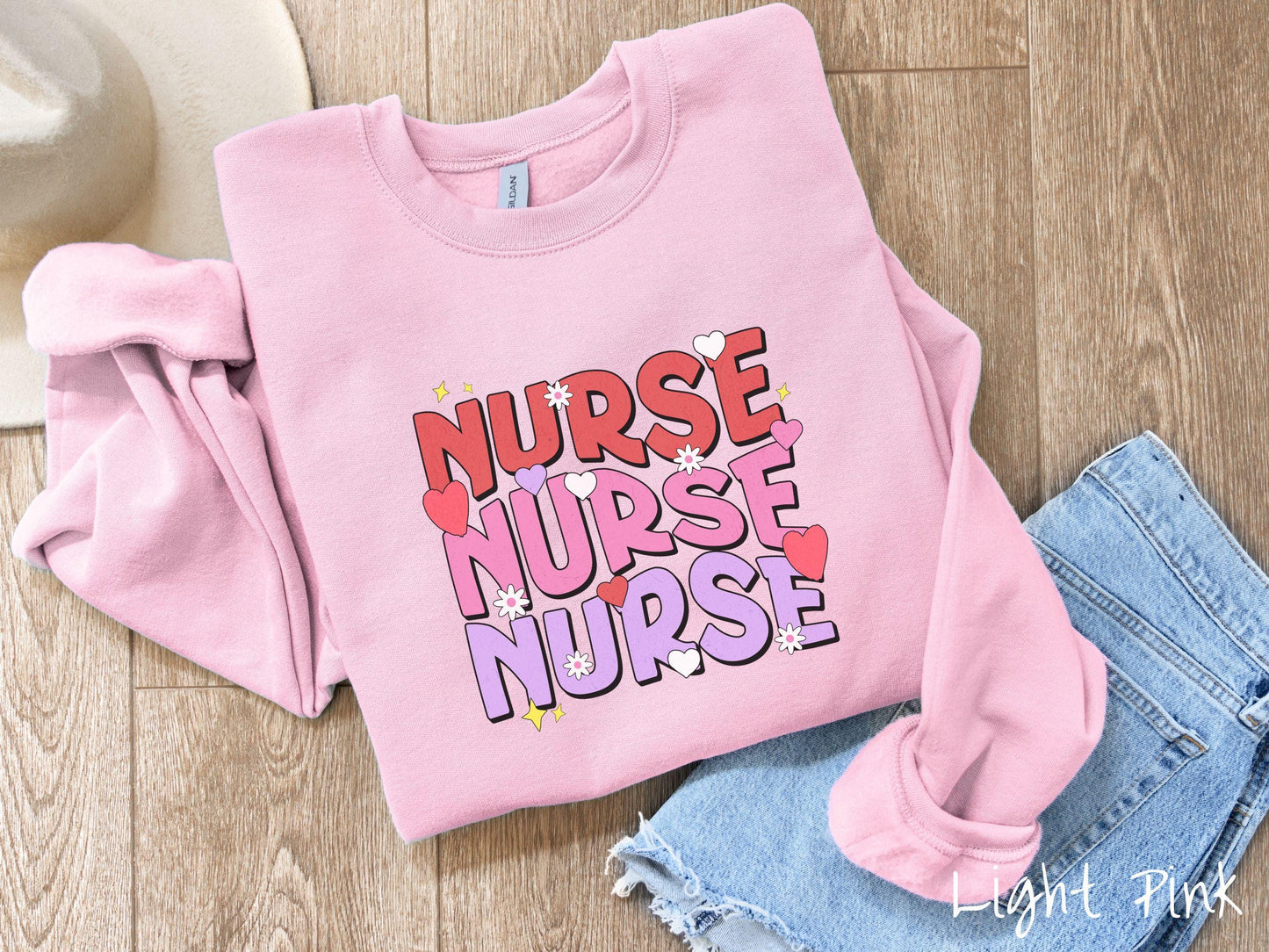 A stylish Gildan Sweatshirt featuring the word "NURSE" written three times vertically in red, pink, and purple font. There are red, white, and purple hearts mixed into the design as well as yellow twinkling stars.