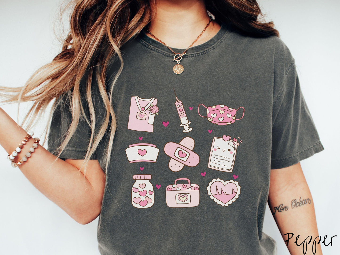 A Comfort Colors T-shirt featuring a 3x3 grid of nursing-themed illustrations adorned with heart designs like nursing scrubs, syringes, a face mask, a nurse cap, bandages, medical records, vitamins, a medical bag, and a heart-shaped EKG graph.