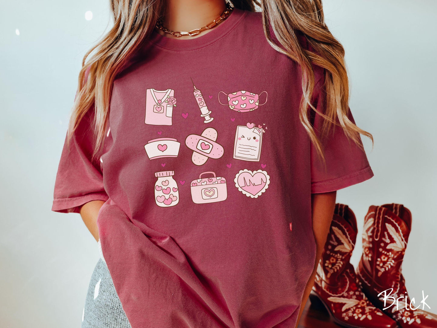 A Comfort Colors T-shirt featuring a 3x3 grid of nursing-themed illustrations adorned with heart designs like nursing scrubs, syringes, a face mask, a nurse cap, bandages, medical records, vitamins, a medical bag, and a heart-shaped EKG graph.