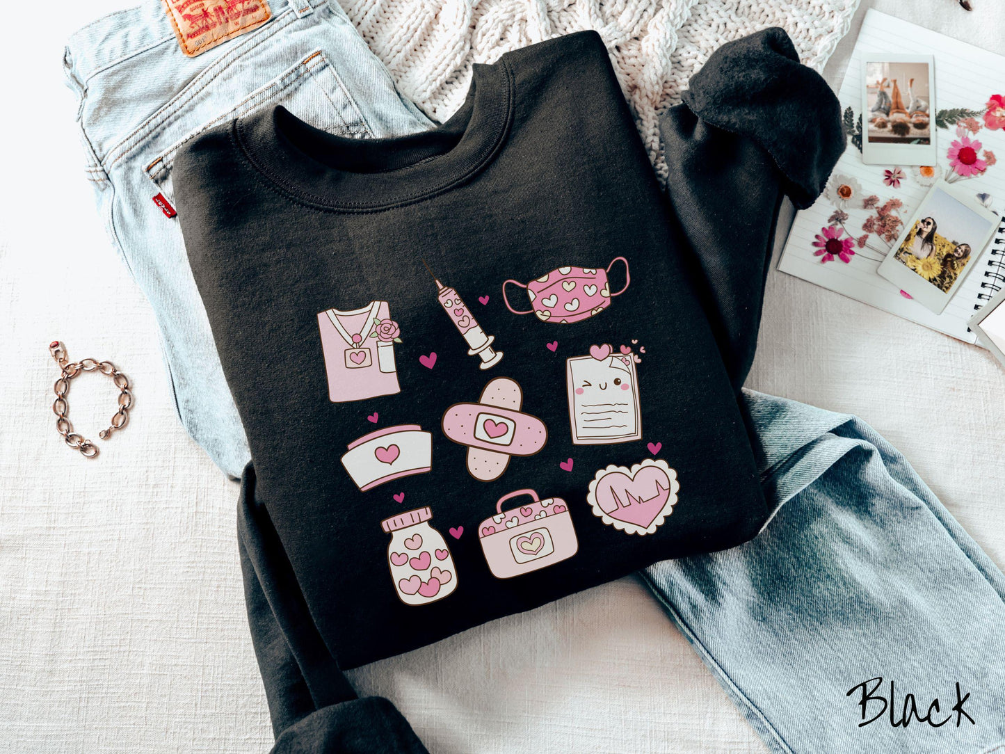 A Gildan sweatshirt featuring a 3x3 grid of nursing-themed illustrations adorned with heart designs like nursing scrubs, syringes, a face mask, a nurse cap, bandages, medical records, vitamins, a medical bag, and a heart-shaped EKG graph.
